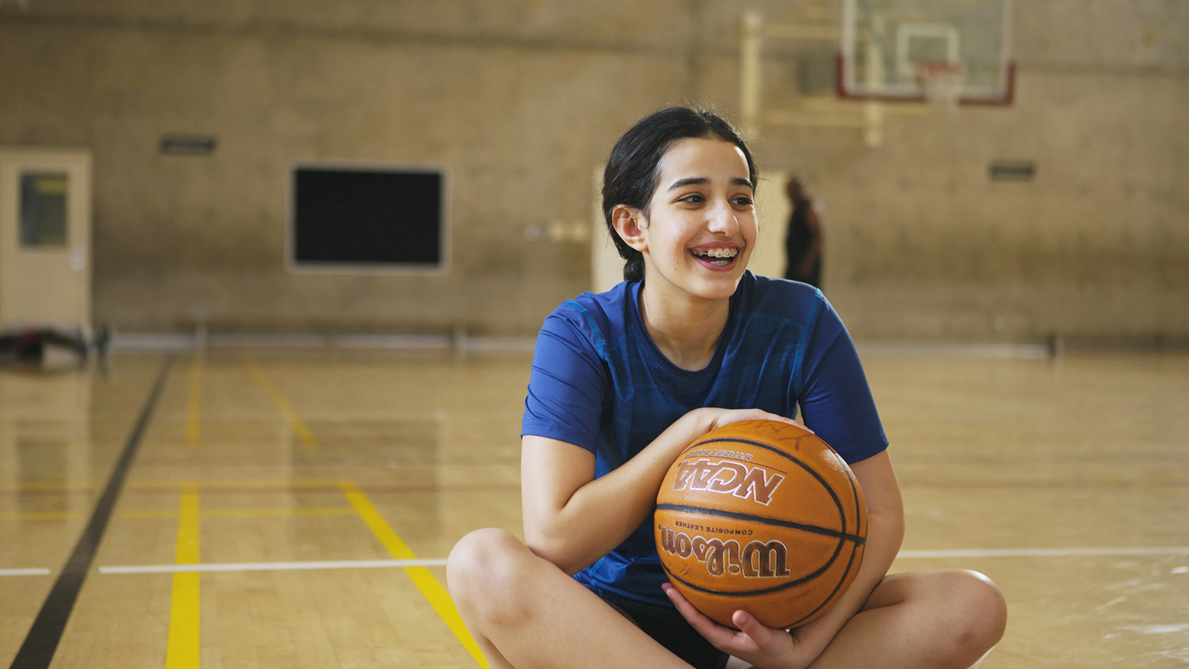 girl sitting in gymnasium with basketball