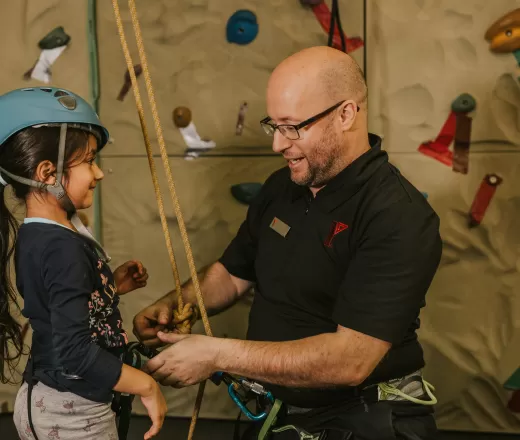 A volunteer helps a young child prepare to climb