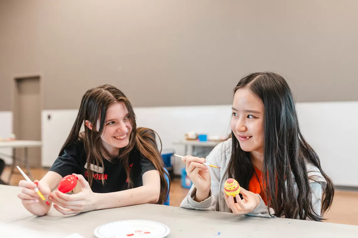 Two girls smiling while painting eggs