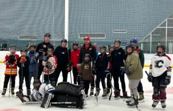 Group of youth wearing hockey gear on the ice smiling with Calgary Flames Forward, Ryan Lomberg